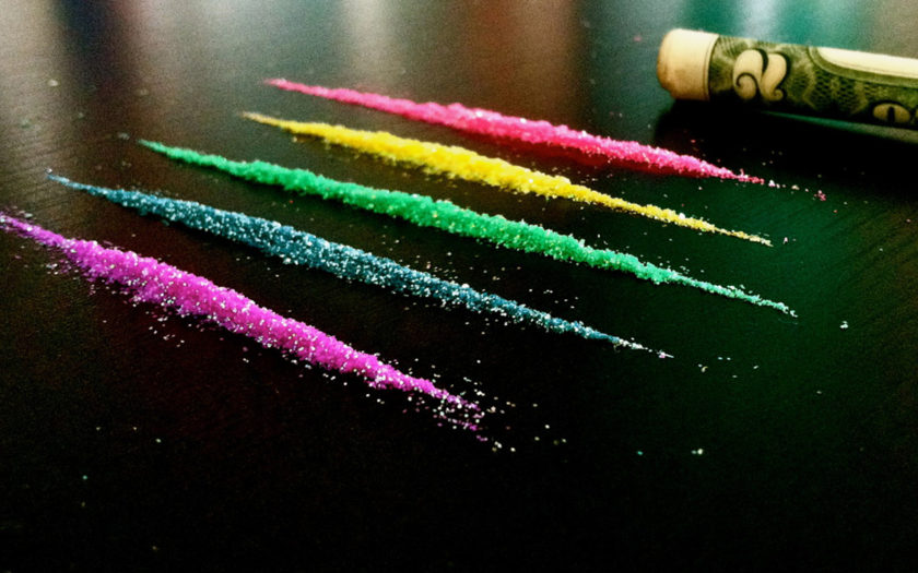 lines of colorful glitter next to a rolled up two dollar bill american