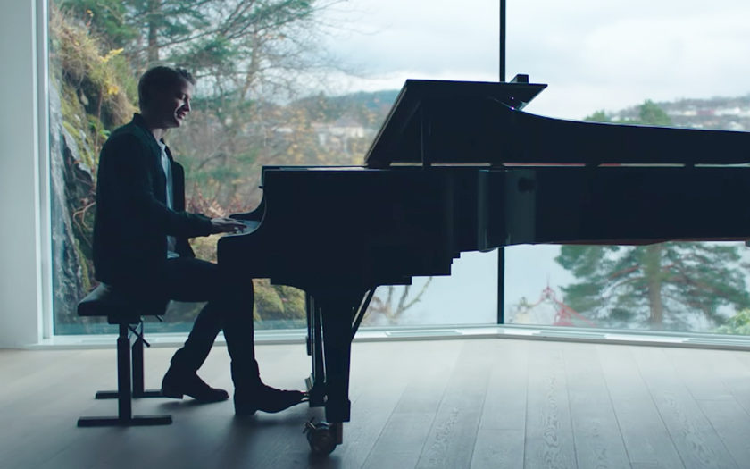 Kygo plays a grand piano in front of a big window with a view of a norwegian bay