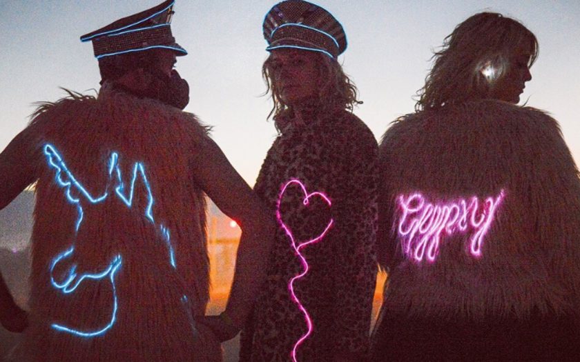 three people wearing neon muse jackets and led captain hats in the desert